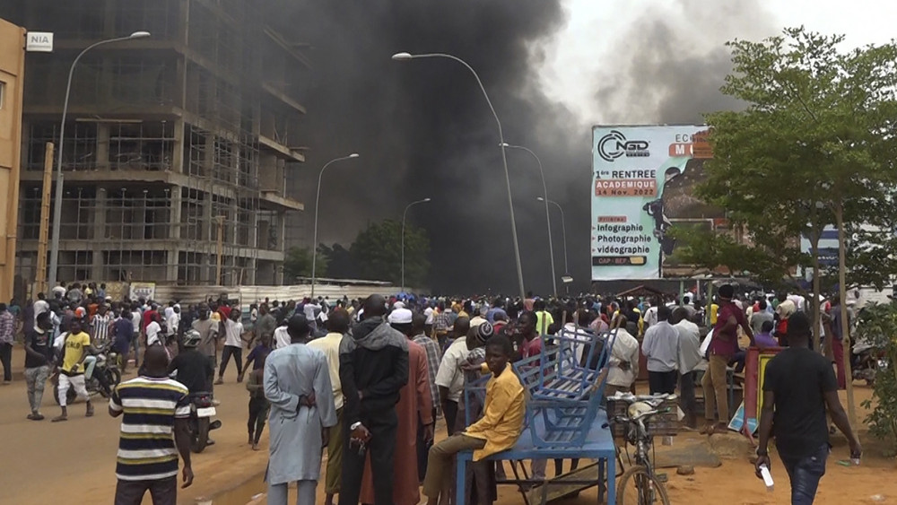 Mit dem brennenden Hauptquartier der Regierungspartei im Rücken demonstrieren Anhänger meuternder Soldaten.