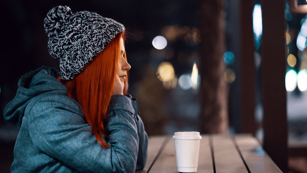 Eine müde Frau trinkt im Winter draußen Kaffee
