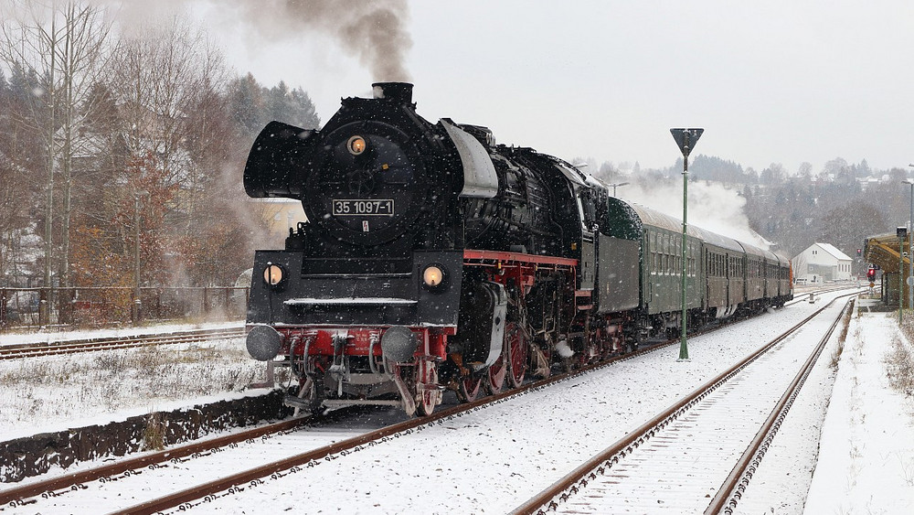 dampflok "julchen" zieht ihre historischen Wagons durch einen verschneiten Bahnhof.