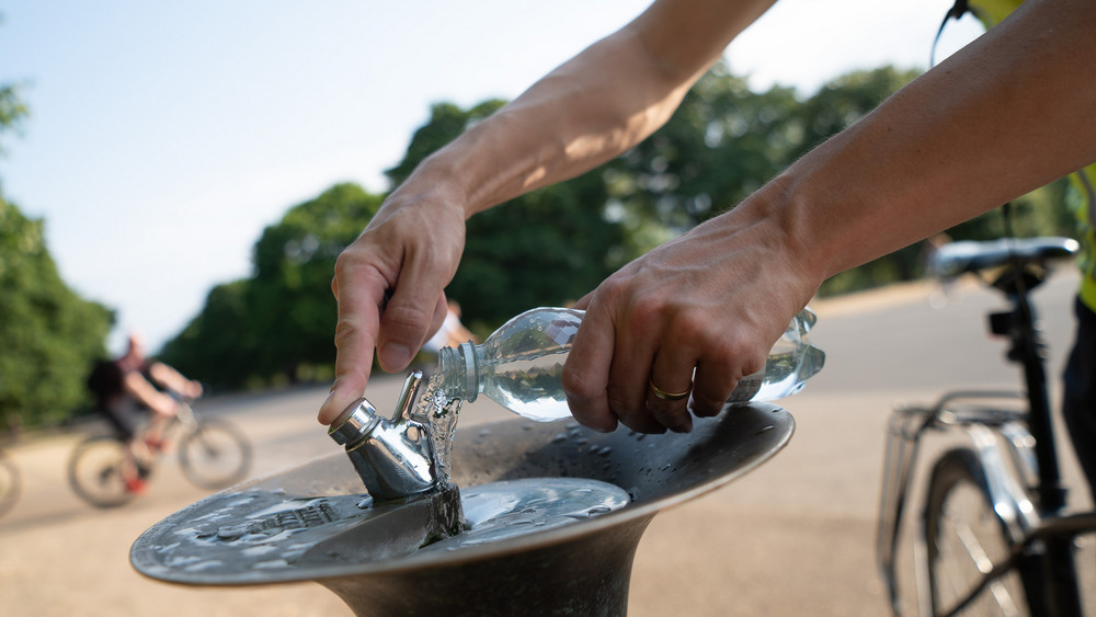 Ein Mann füllt an einem Trinkbrunnen seine Wasserflasche auf.