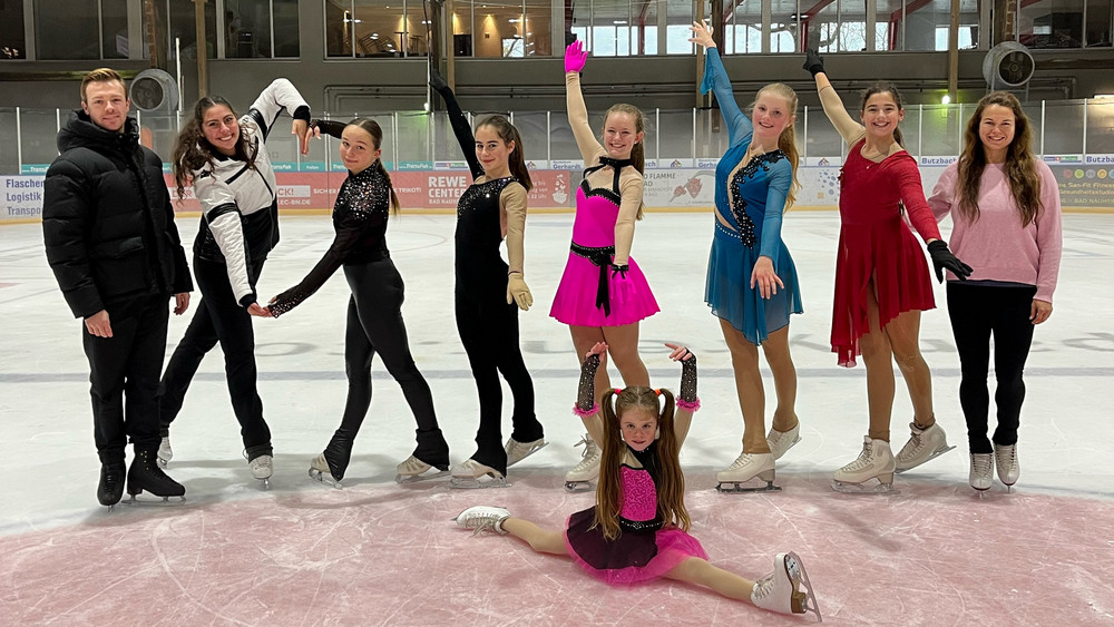 Die jungen Eiskunstläuferinnen präsentieren sich in der Eishalle zusammen mit ihren Trainern.