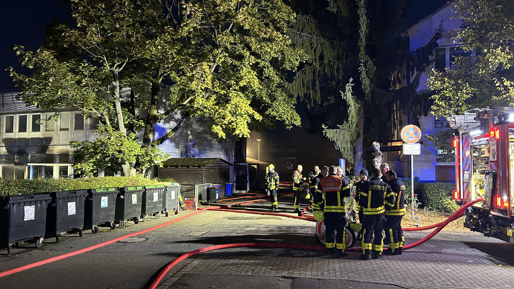 Eine Straße bei Nacht. Feuerwehrleute bedienen ein Löschfahrzeug.
