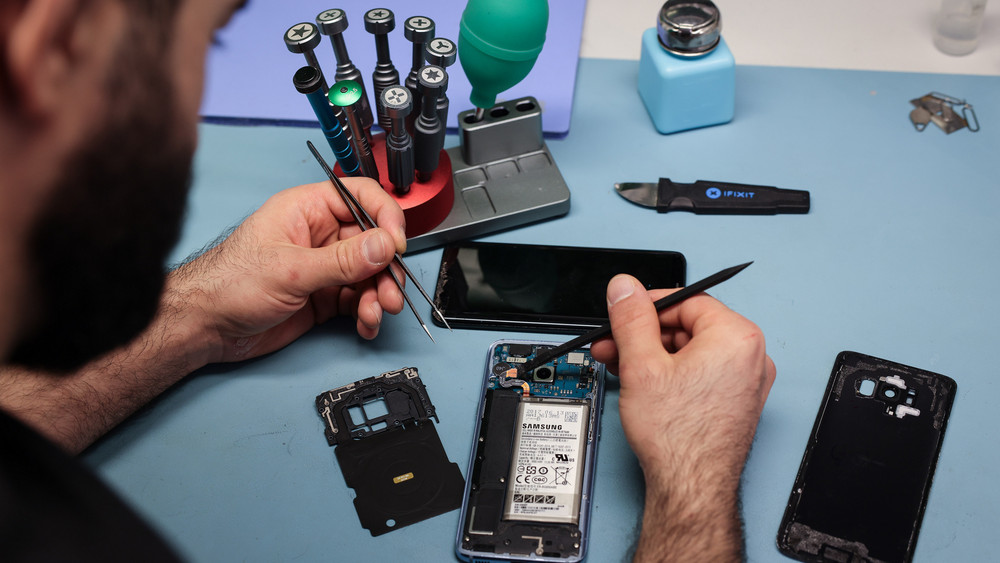 Ein Techniker arbeitet an einem Smartphone mit defektem Display in seinem kleinen Fachgeschäft für Reparaturen und Zubehör. In der EU sollen Kunden in Zukunft das Recht haben, bestimmte Geräte reparieren zu lassen.