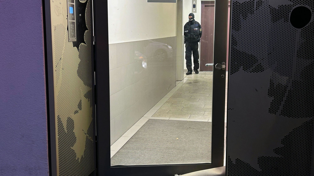 Ein Polizeibeamter steht bei einer Razzia in Berlin-Adlershof im Eingangsbereich eines Gebäudes.