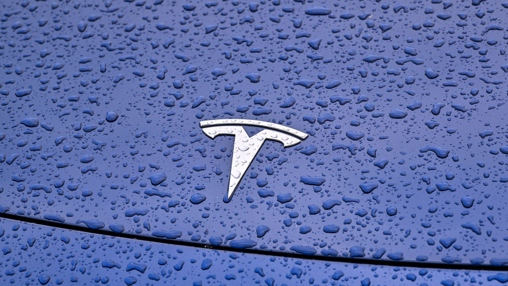 Regentropfen sind auf einem Pkw mit dem Tesla-Symbol vor dem Werk der Tesla-Autofabrik zu sehen. Der angekündigte Personalabbau bei Tesla trifft auch das einzige europäische Werk bei Berlin. Details bleiben unklar. Es sollen aber weit weniger als 3000 Stellen betroffen sein.