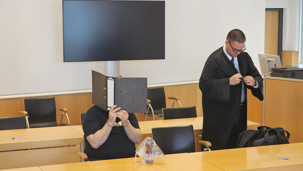 Der angeklagte 50-Jährige verhüllt vor Prozessbeginn sein Gesicht mit einem Ordner.