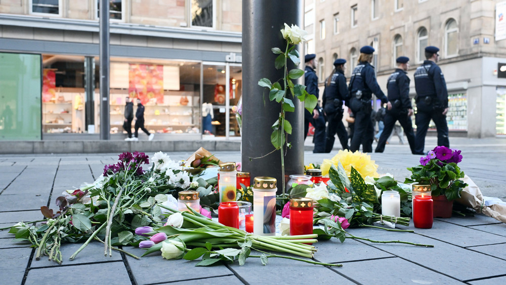 Blumen zum Gedenken an die Opfer liegen an einer Straßenlaterne, im Hintergrund Polizei