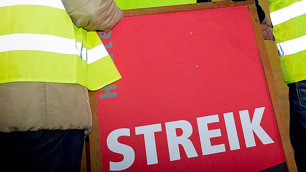 Zwei Menschen in Warnwesten mit Streik-Schild